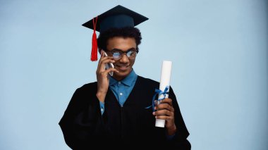 Mezuniyet elbisesi ve şapkası olan Afro-Amerikan gençleri mavi telefonda konuşurken ellerinde diploma tutuyorlar.