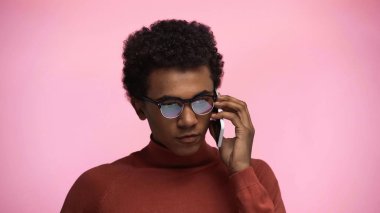 Balıkçı yaka kazaklı ve gözlüklü Afro-Amerikan ergen pembe bir cep telefonuyla konuşuyor.