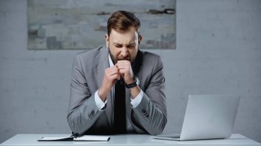 tired businessman in suit yawning and covering mouth with clenched fist 