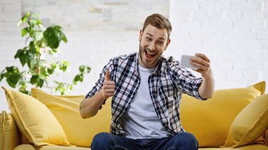 excited man taking selfie on mobile phone while showing thumb up