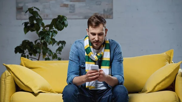 Young Bearded Man Scarf Sitting Sofa Looking Smartphone — Stok fotoğraf