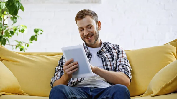 Cheerful Bearded Man Using Digital Tablet While Sitting Couch — Stok fotoğraf
