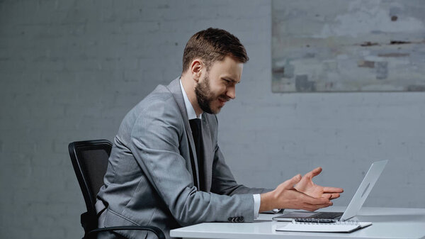 недовольный молодой бизнесмен жестикулирует, глядя на ноутбук