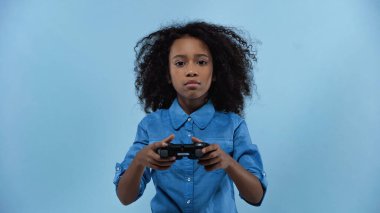 KYIV, UKRAINE - MARCH 02, 2021: curly african american girl holding gamepad isolated on blue