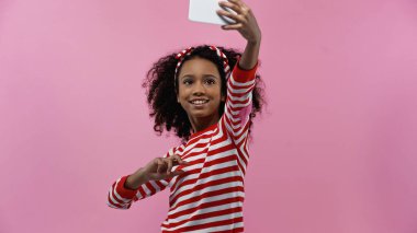 smiling african american girl taking selfie isolated on pink
