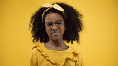 curly african american girl in glasses sticking out tongue isolated on yellow