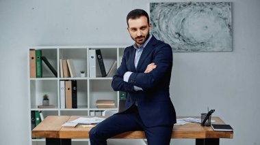 Ofisteki çalışma masasının yanındaki kameraya bakan kendine güvenen iş adamı. 