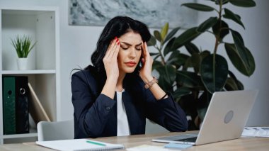 Ofiste dizüstü bilgisayarın yanında baş ağrısı çeken iş kadını 