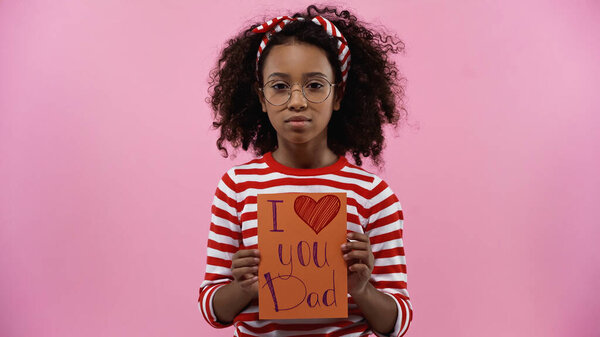 вьющиеся африканские американская девушка в очках держа поздравительную открытку с я люблю тебя папа буквы изолированы на розовый