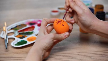 cropped view of woman painting orange easter egg 