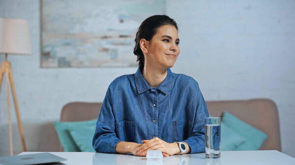 cheerful woman looking away neat glass of water on desk