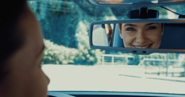 blurred and happy woman smiling while looking in rearview mirror clipart