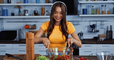 Kablosuz kulaklıklı mutlu kadın müzik dinliyor ve salata karıştırıyor.
