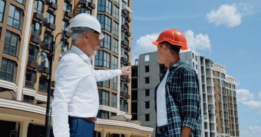 mature engineer pointing with finger near builder on construction site clipart