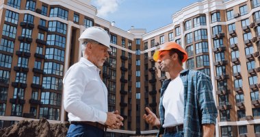 low angle view of engineer and builder talking near new building clipart