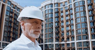 middle aged engineer looking away near building on background  clipart