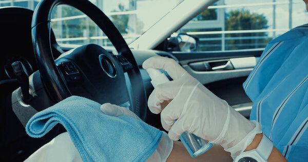 cropped view of woman in latex gloves spraying sanitizer on rag