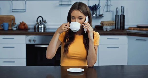 young woman drinking coffee and talking on smartphone