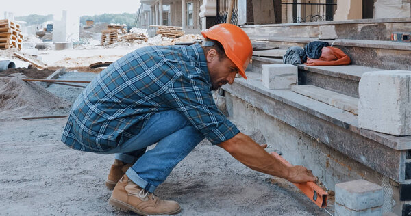 Builder in hard hat holding building level on construction site