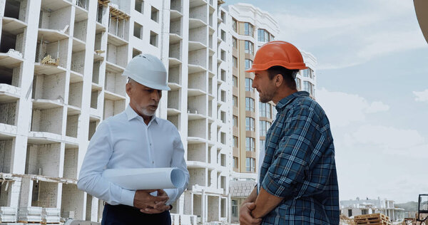 Engineer with blueprints having conversation with builder on construction site