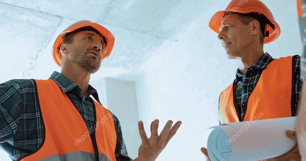  builder in hard hat gesturing while talking on construction site