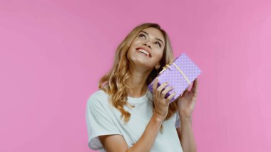Gülümseyen sarışın kadın pembe bir hediye kutusu tutuyor.