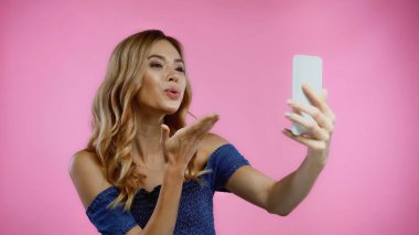 Mutlu genç bir kadın pembe bir selfie çekerken havada öpüşüyor. 