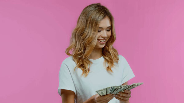 веселая блондинка в белой футболке с долларами, изолированными на розовый