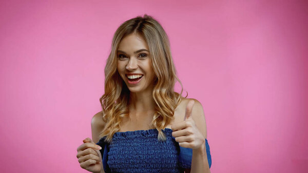 cheerful young woman showing thumb up on pink 