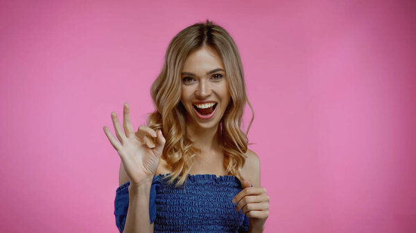 cheerful young woman showing okay sign on pink 