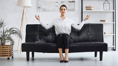 Başarılı iş kadını ofiste koltukta otururken meditasyon yapıyor.