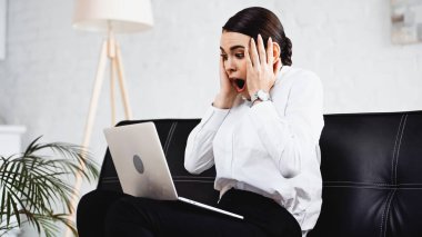 Şok olmuş iş kadını dizüstü bilgisayarla koltukta otururken kafasına dokunuyor