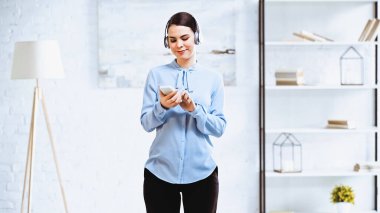 Kablosuz kulaklıkla müzik dinlerken akıllı telefon kullanan neşeli iş kadını.