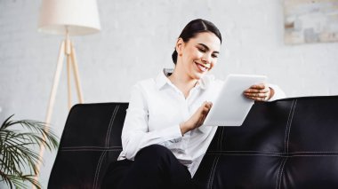 Ofisteki koltukta dijital tablet kullanan neşeli iş kadını.