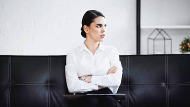 Kollarını kavuşturup kanepede oturan düşünceli bir iş kadını.