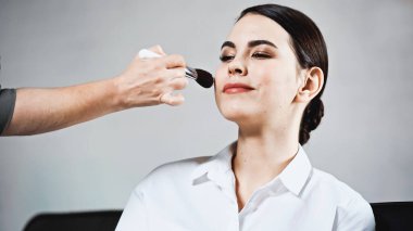 Makyaj sanatçısı gülümseyen modele yüz pudrası uyguluyor