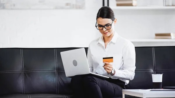 young businesswoman sitting on couch with laptop and credit card