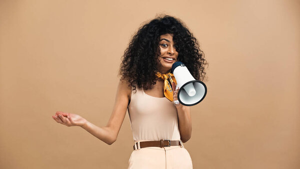 Веселая латиноамериканка держит громкоговоритель изолированным на бежевом 