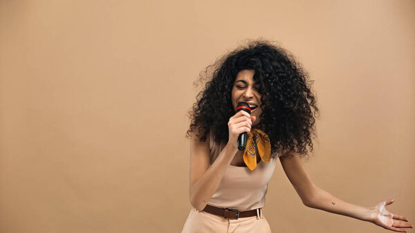 hispanic woman singing in microphone isolated on beige 