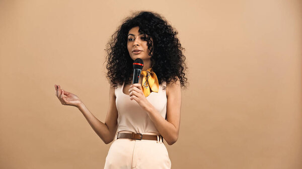 латиноамериканка держит микрофон изолированным на бежевый 
