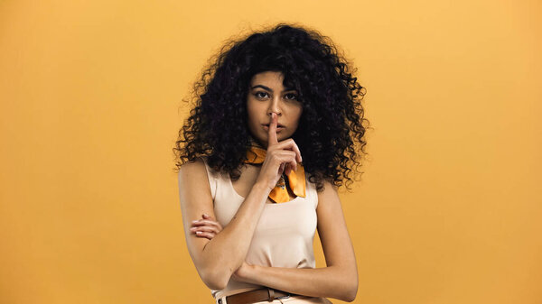 латиноамериканка, показывающая тайный жест перед камерой, изолированной на желтом