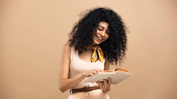 Веселая латиноамериканка читает книгу, изолированную от бежевого 