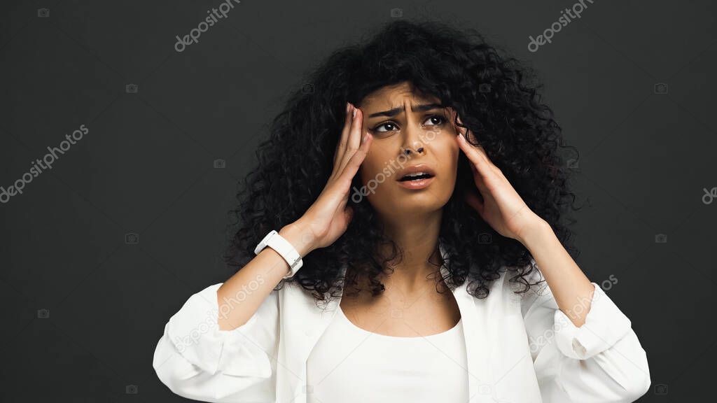 Stressed hispanic woman with hands near head isolated on black 