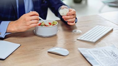 Paket salatasının yanında plastik çatal tutan işadamı manzarası. 