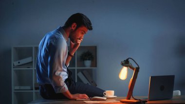 businessman looking at laptop while working late in office clipart