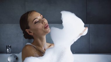 Genç kadın banyo yapıyor ve beyaz köpük üflüyor. 