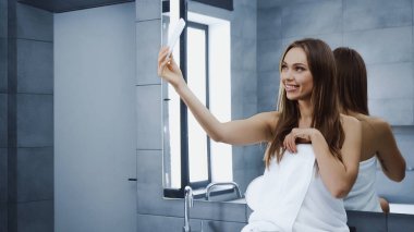 Havlulu neşeli genç kadın banyoda selfie çekiyor.