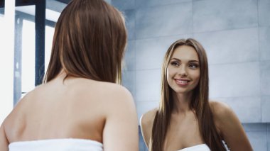 Neşeli genç kadın aynaya bakıyor ve banyoda gülümsüyor. 