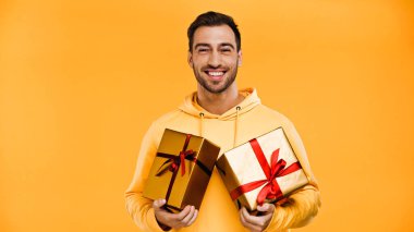 cheerful man holding wrapped gifts isolated on yellow clipart