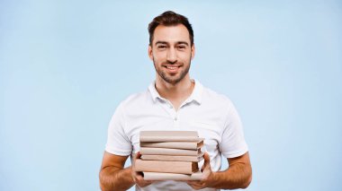 cheerful man holding pile of books isolated on blue clipart